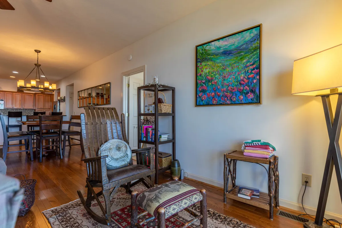 A warm, intimate corner of the cabin featuring a comfortable rocking chair next to a colorful painting and a wooden shelf, softly illuminated by a floor lamp. The cozy setting suggests a peaceful nook for quiet moments, reading, or sharing conversation.
