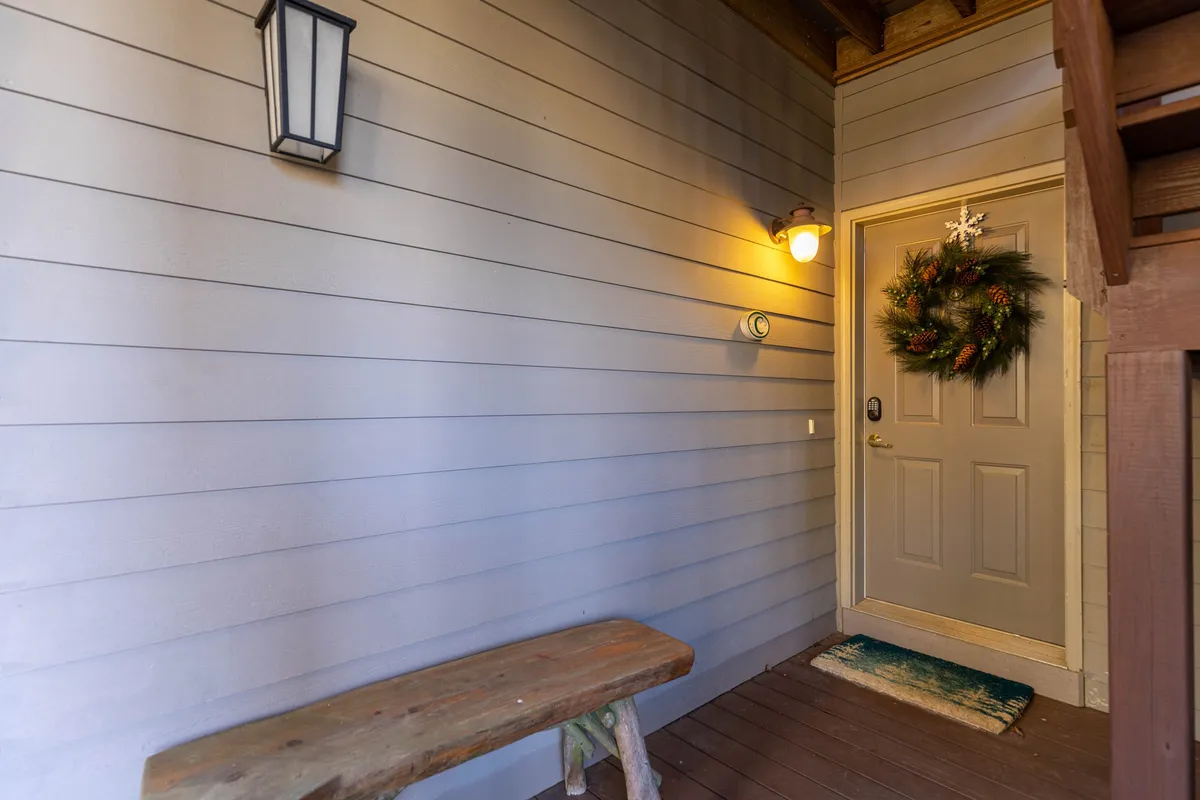 A welcoming entry area featuring a decorative wreath on the front door, a comfortable bench alongside, and a wall lantern creating a cozy, inviting atmosphere. The scene suggests a warm greeting for guests arriving at the condo and hints at the privacy and tucked-away nature of the unit.