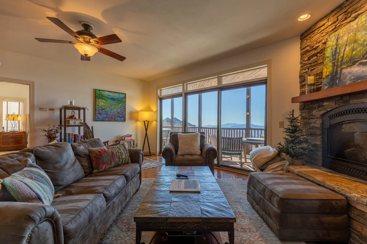This image showcases a cozy living room with a comfortable sofa facing a stone gas fireplace. Large windows dominate one wall, offering sweeping views of the Blue Ridge Mountains. Artwork and a coffee table add inviting touches, and the natural light enhances the room's warm, welcoming ambiance.