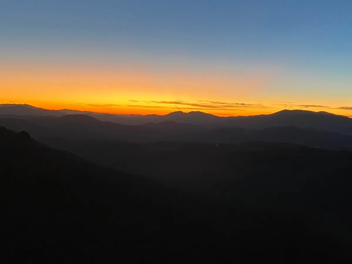 This view image captures a dramatic sunset with mountain silhouettes and a gradient sky, evoking a serene atmosphere ideal for photography, stargazing, and quiet reflection. The expansive horizon embodies the natural beauty of the region at golden hour.