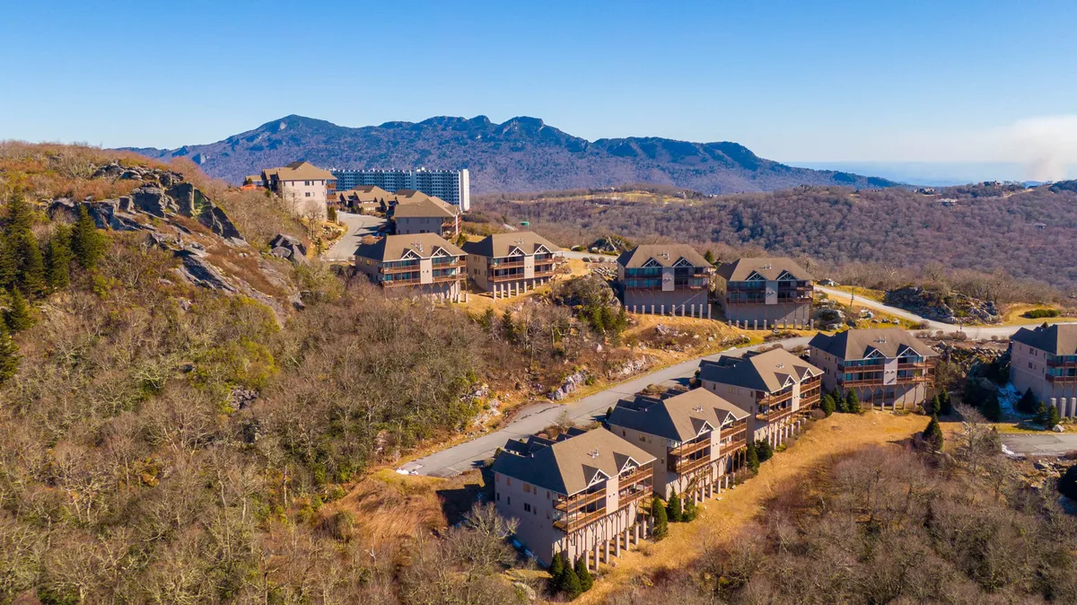 This exterior image showcases a tranquil mountain range with residential buildings nestled in the open landscape, capturing the atmosphere of Sugar Mountain and its proximity to outdoor adventure. The view highlights the natural terrain, evoking the excitement of ski slopes in winter or mountain biking trails in warmer months.