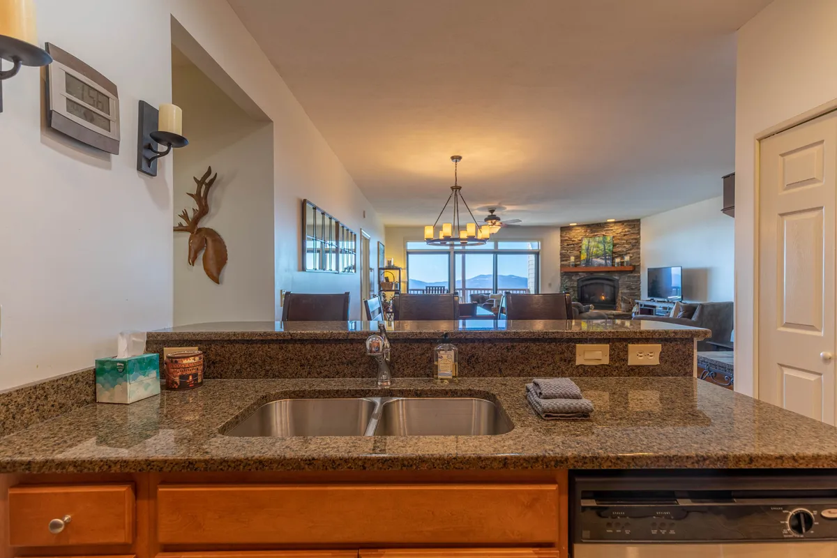 This image captures the open-concept living area featuring a granite countertop, a spacious dining area beside large windows, and a cozy fireplace. The scene suggests a space ideal for family gatherings, enjoying meals with mountain sunset views, and relaxing evenings together.