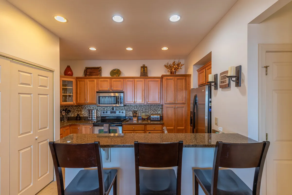 A welcoming kitchen scene featuring spacious granite countertops, sleek stainless steel appliances, and inviting wood cabinetry. Decorative items on the shelves add a homey touch, while the ample counter space is perfect for meal prep and socializing.