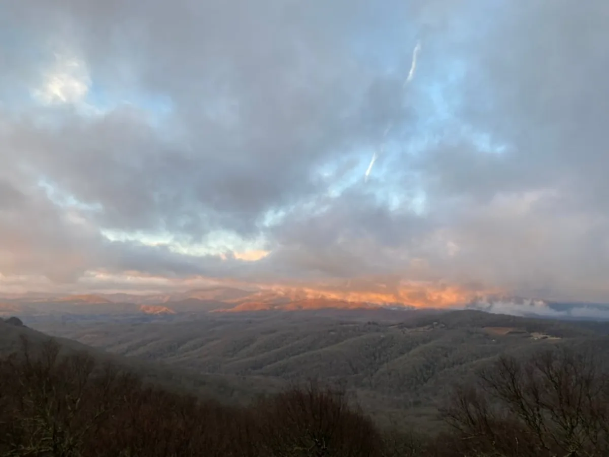 A sweeping view of a mountain range under a glowing sunset, with dramatic clouds and open wilderness. The image evokes a sense of serenity and awe, inviting guests to imagine the thrill of mountain adventures and the beauty waiting just beyond their doorstep.