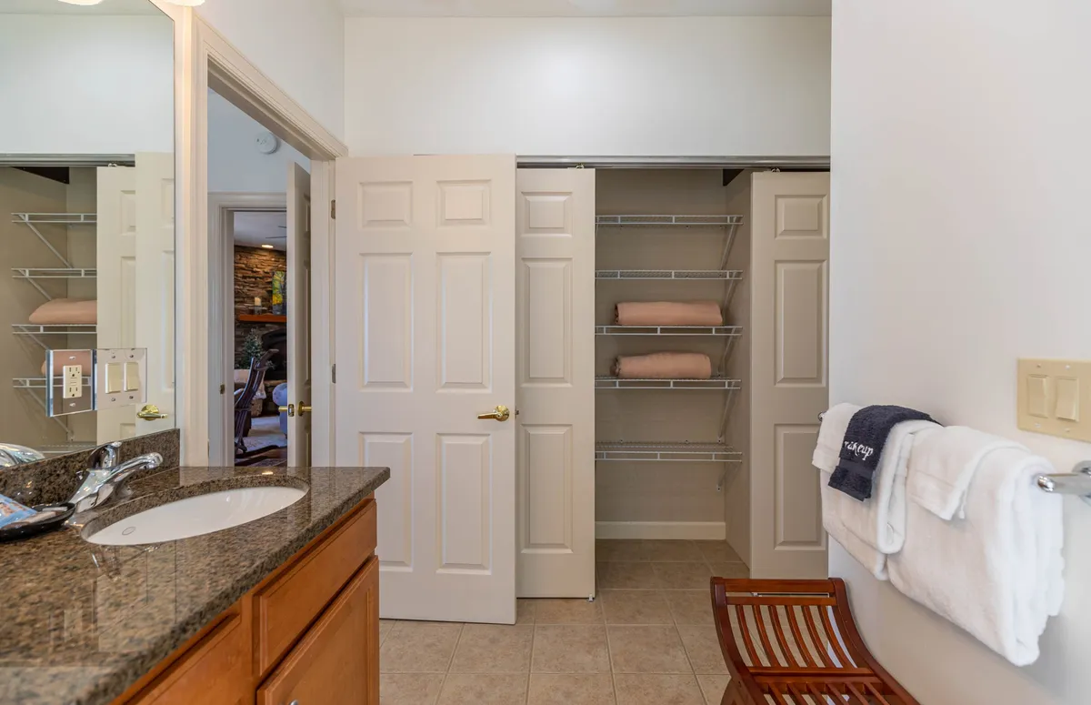 A stylish interior space with a granite countertop, double doors leading to a closet, and neat towels hanging on a rack. The wooden chair and overall organization create an inviting, upscale atmosphere.