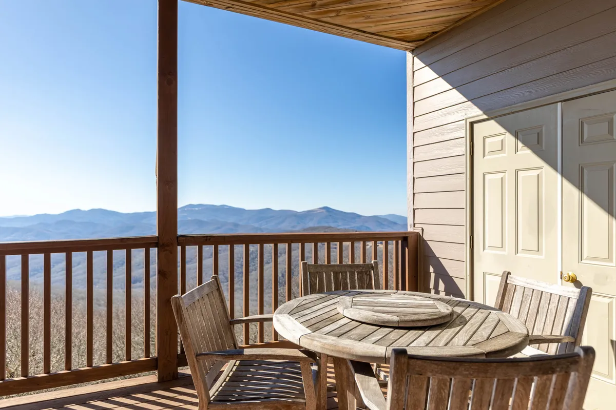 An outdoor space with a sturdy wooden table and chairs set against railings, offering expansive mountain views. The scene evokes the perfect spot for relaxing after a day on the slopes or trails, with the sky hinting at sunrise or sunset, adding to the authentic mountain ambiance.